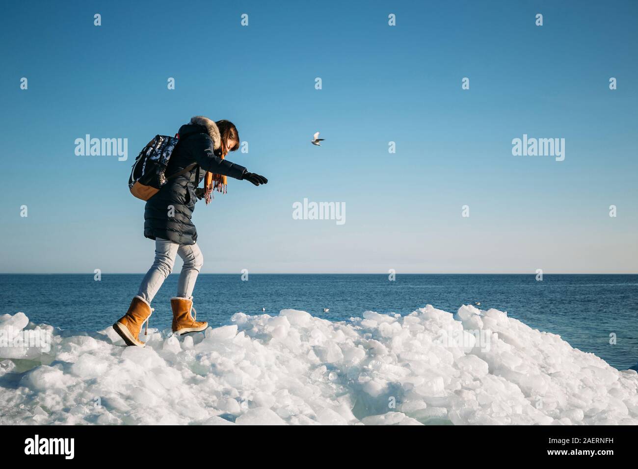 Giovane donna sorridente camminando su una parte superiore del mare congelato i blocchi di ghiaccio su una costa del mare con un cielo blu sullo sfondo, al gelido giorno soleggiato Foto Stock
