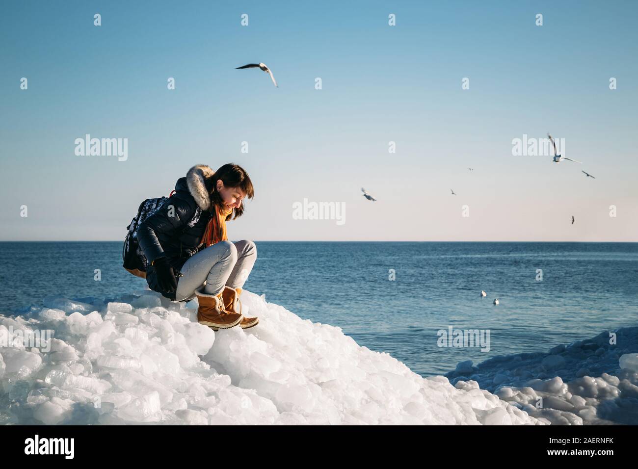 Giovane donna sorridente seduto su una parte superiore del mare congelato i blocchi di ghiaccio su una costa del mare con un cielo blu sullo sfondo, al gelido giorno soleggiato Foto Stock