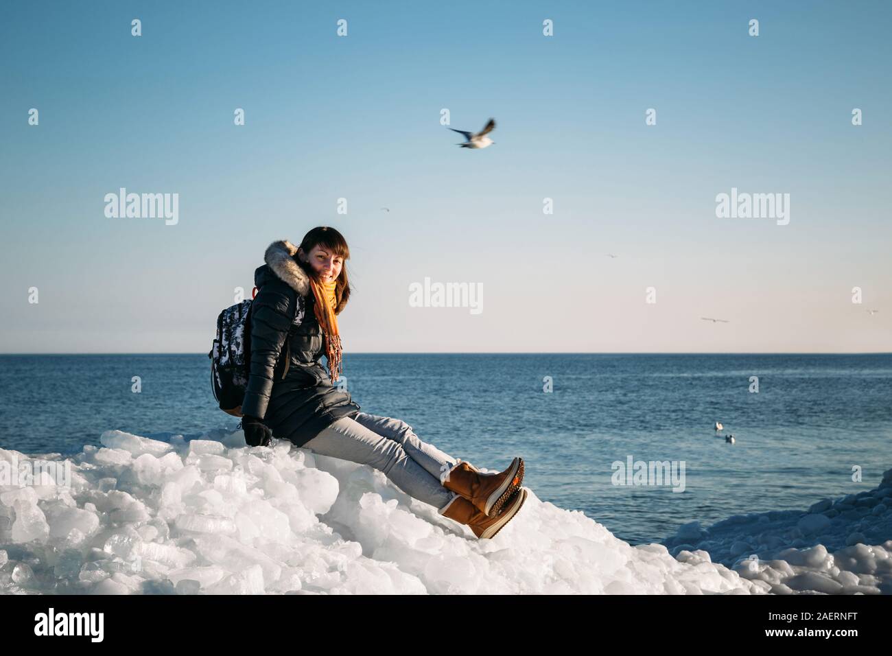 Giovane donna sorridente seduto su una parte superiore del mare congelato i blocchi di ghiaccio su una costa del mare con un cielo blu sullo sfondo, al gelido giorno soleggiato Foto Stock