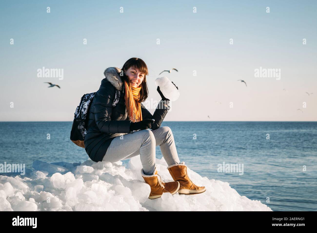 Giovane donna sorridente seduto sulla cima del mare i blocchi di ghiaccio sulla costa azienda rotto pezzo di ghiaccio, con il blu del mare e del cielo e lo sfondo Foto Stock