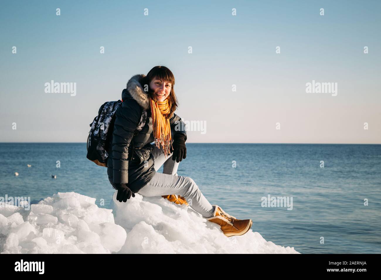 Giovane donna sorridente seduto su una parte superiore del mare congelato i blocchi di ghiaccio su una costa del mare con un cielo blu sullo sfondo, al gelido giorno soleggiato Foto Stock