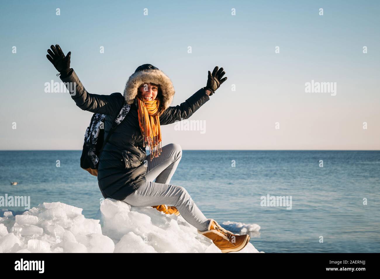 Giovane donna sorridente seduto su una parte superiore del mare congelato i blocchi di ghiaccio su una costa del mare con un cielo blu sullo sfondo, al gelido giorno soleggiato Foto Stock