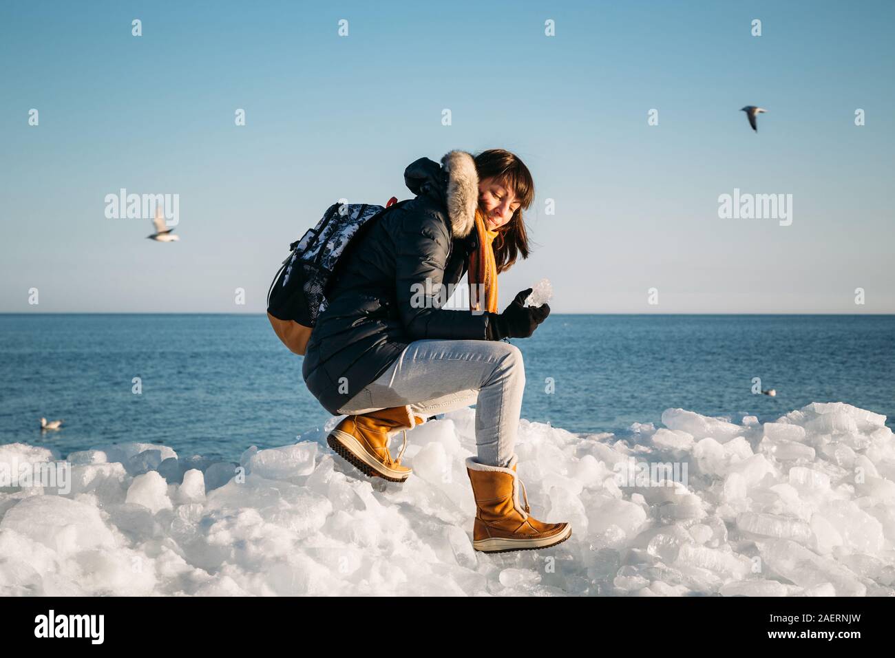 Giovane donna sorridente seduto sulla cima del mare i blocchi di ghiaccio sulla costa azienda rotto pezzo di ghiaccio, con il blu del mare e del cielo e lo sfondo Foto Stock
