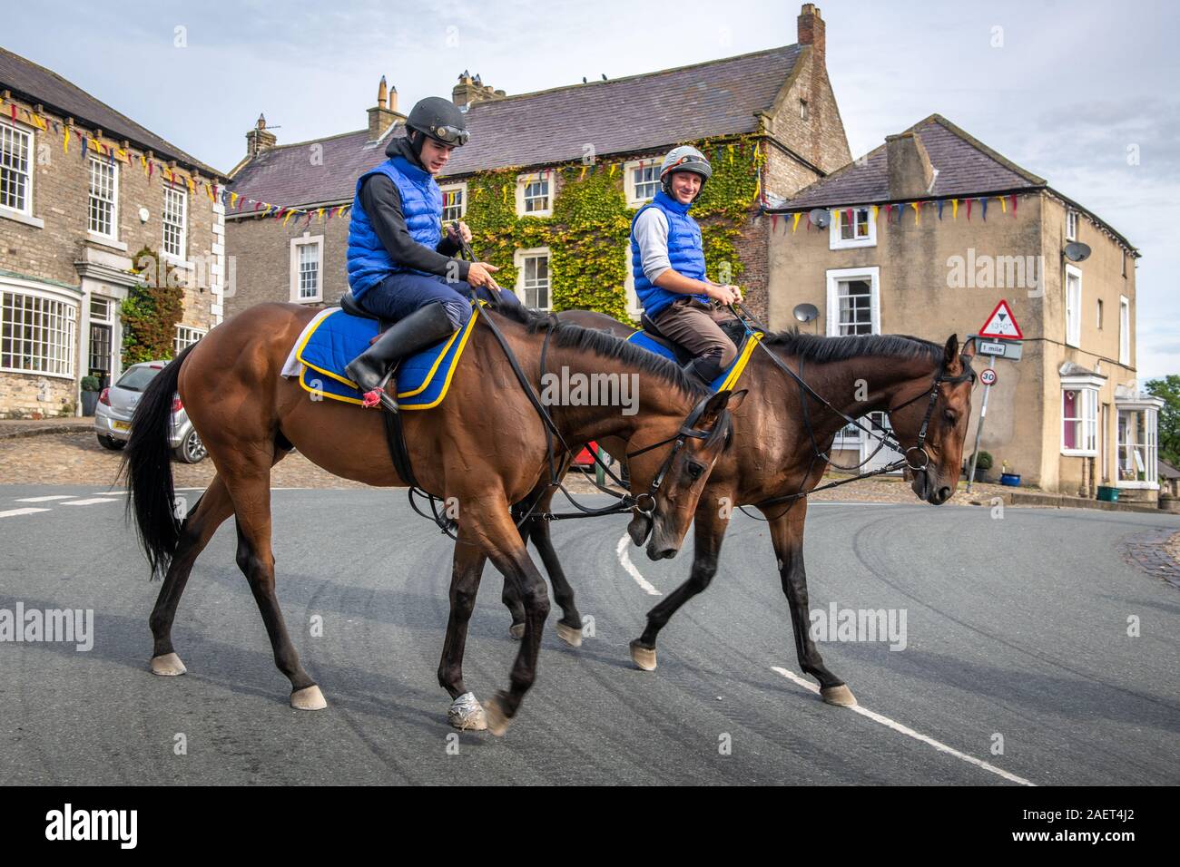 Middleham, Inghilterra - un gruppo di equestrians cavalcare lungo un piccolo villaggio street, Yorkshire, Regno Unito Foto Stock