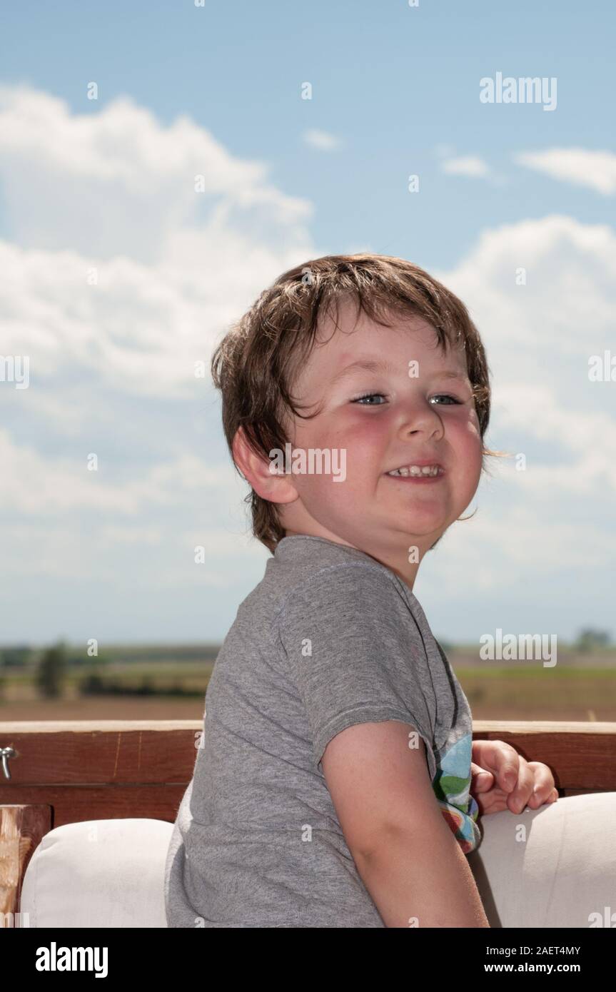 Un felice little boy sorridere mentre in piedi su una sedia sulla piattaforma esterna Foto Stock