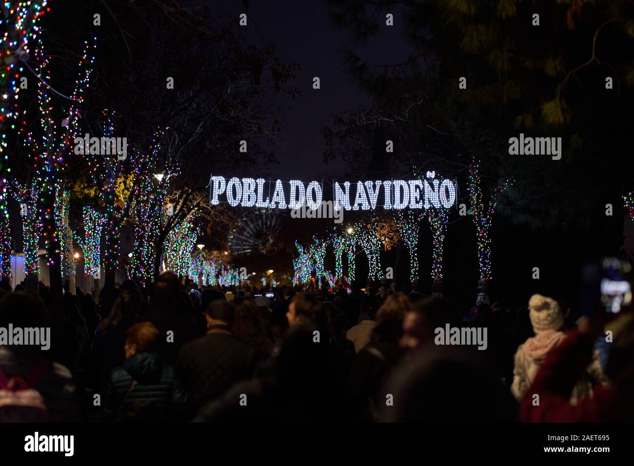 Le folle di persone passano sotto il cartello illuminato per la sezione del villaggio di Natale della Fiera di Natale a Torrejon de Ardoz Foto Stock