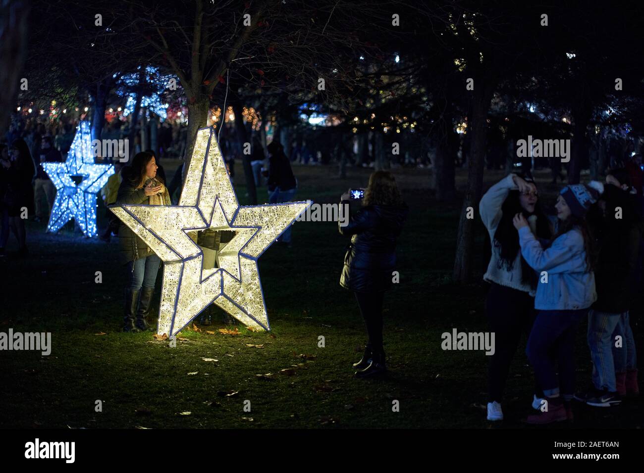 Giovani donne che posano per una foto accanto a una luce a forma di stella dorata luminosa in un parco di notte, Torrejón de Ardoz, Spagna Foto Stock