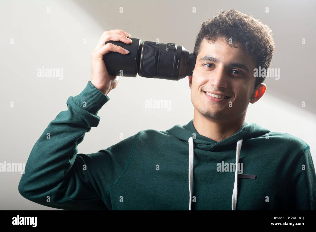 Giovane uomo verde da indossare pullover e tenendo un obiettivo macro sul lato destro della sua testa davanti a sfondo grigio chiaro Foto Stock