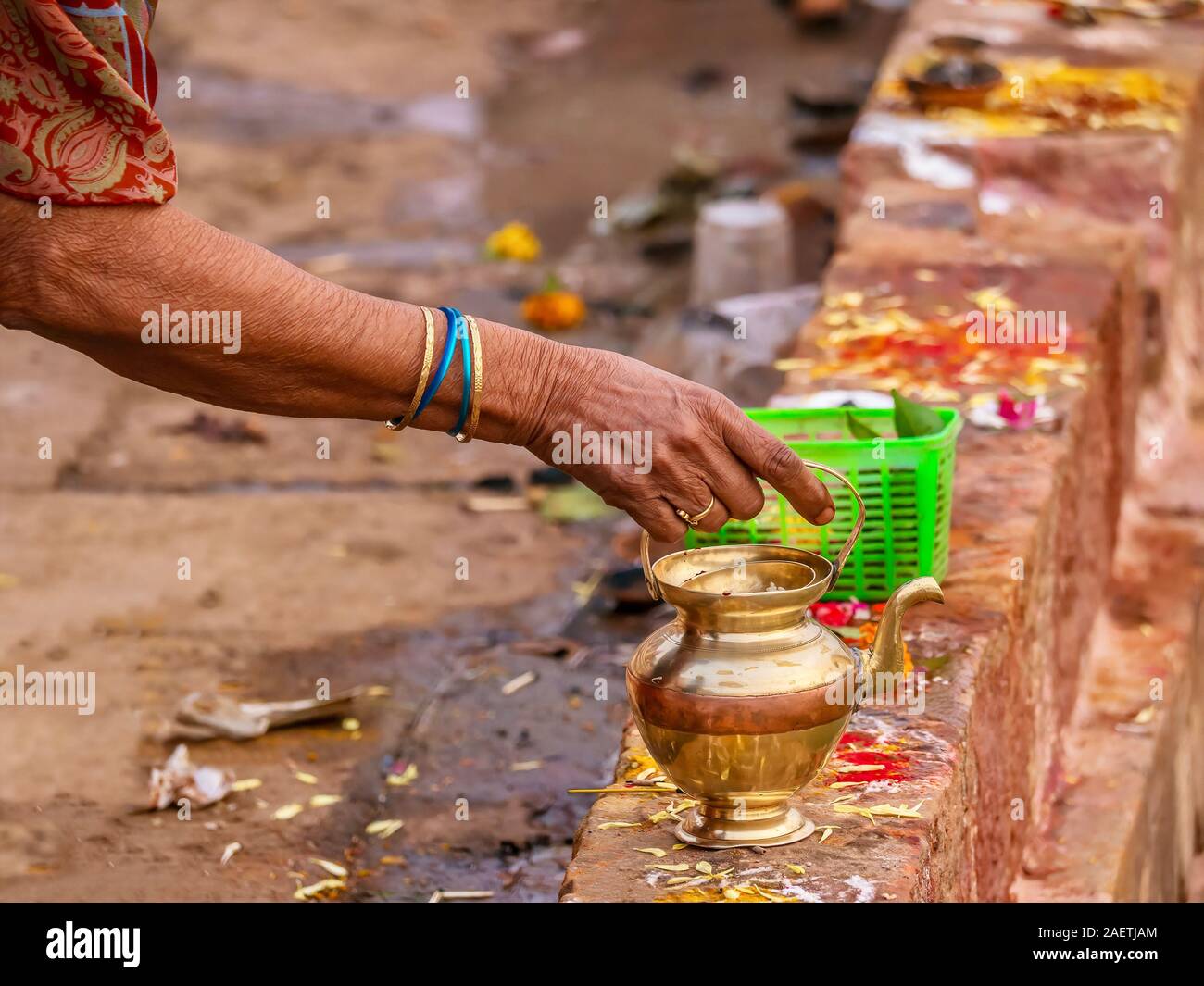 Una donna si prepara un'offerta personale a una divinità Indù utilizzando un recipiente di ottone, un cestello di betel foglie e frutti e kumkum colorato in polvere. Foto Stock