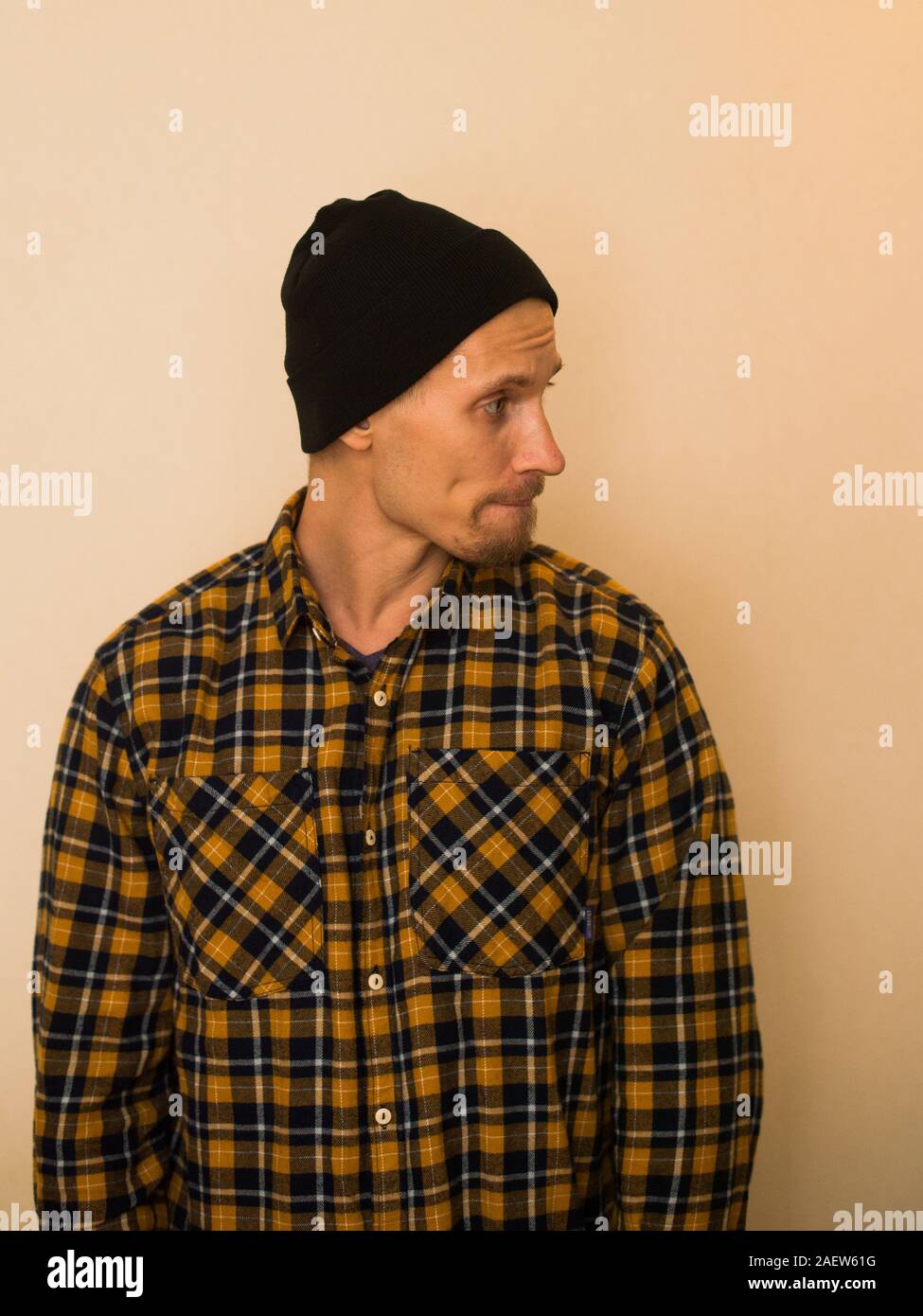 Un giovane ragazzo in un plaid shirt pone contro un muro beige. Modello in abiti di tutti i giorni. Elegante uomo giovane. Foto Stock