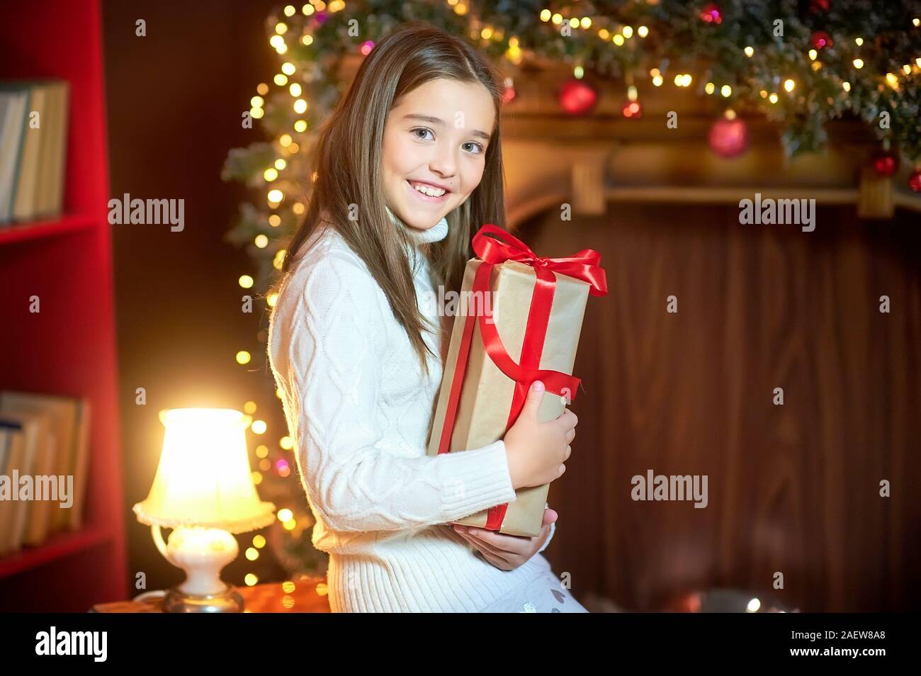 Bella ragazza di sera in camera contiene un regalo avvolto in nastro rosso e sorrisi. Vacanze a. Natale e Anno Nuovo. Foto Stock