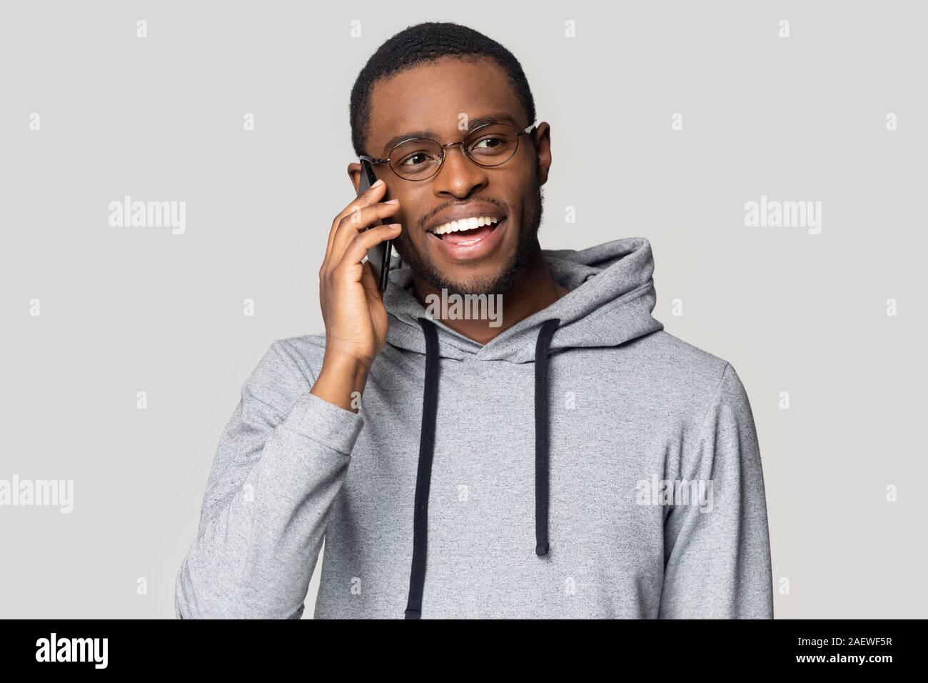 Eccitato giovane ragazzo nero in occhiali chat sul telefono cellulare. Foto Stock