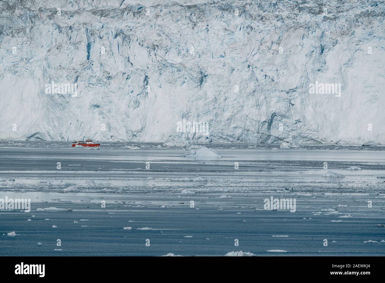 Passeggero rosso la nave di crociera in barca a vela attraverso le acque ghiacciate di Qasigiannguit, Groenlandia con Eqip Eqi Sermia ghiacciaio in background. Una piccola barca tra Foto Stock