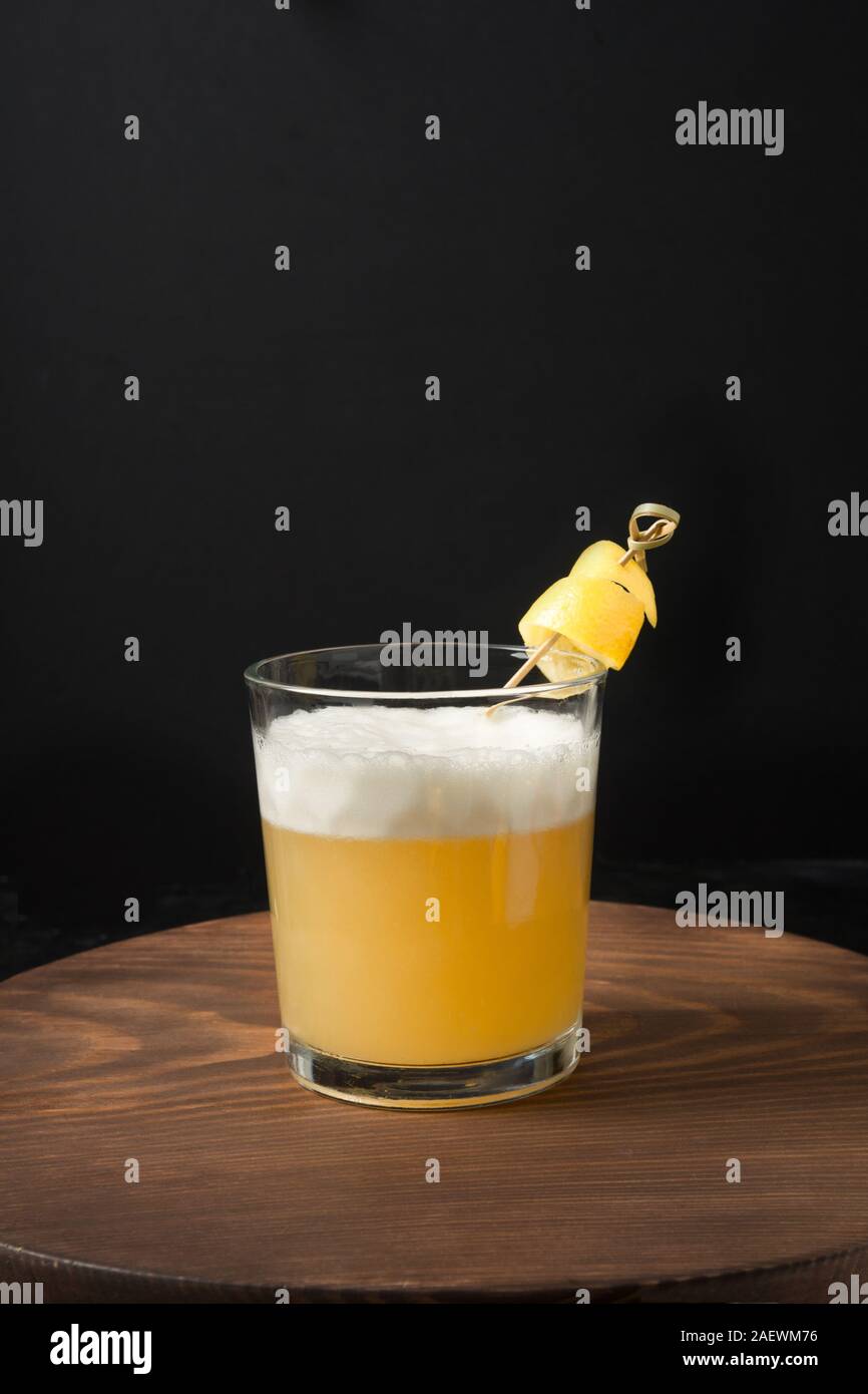 Uno shot di whiskey sour cocktail - bourbon con il succo di limone e lo sciroppo di zucchero e albume in vetro su tavola di legno sul nero. Orientamento verticale. Foto Stock