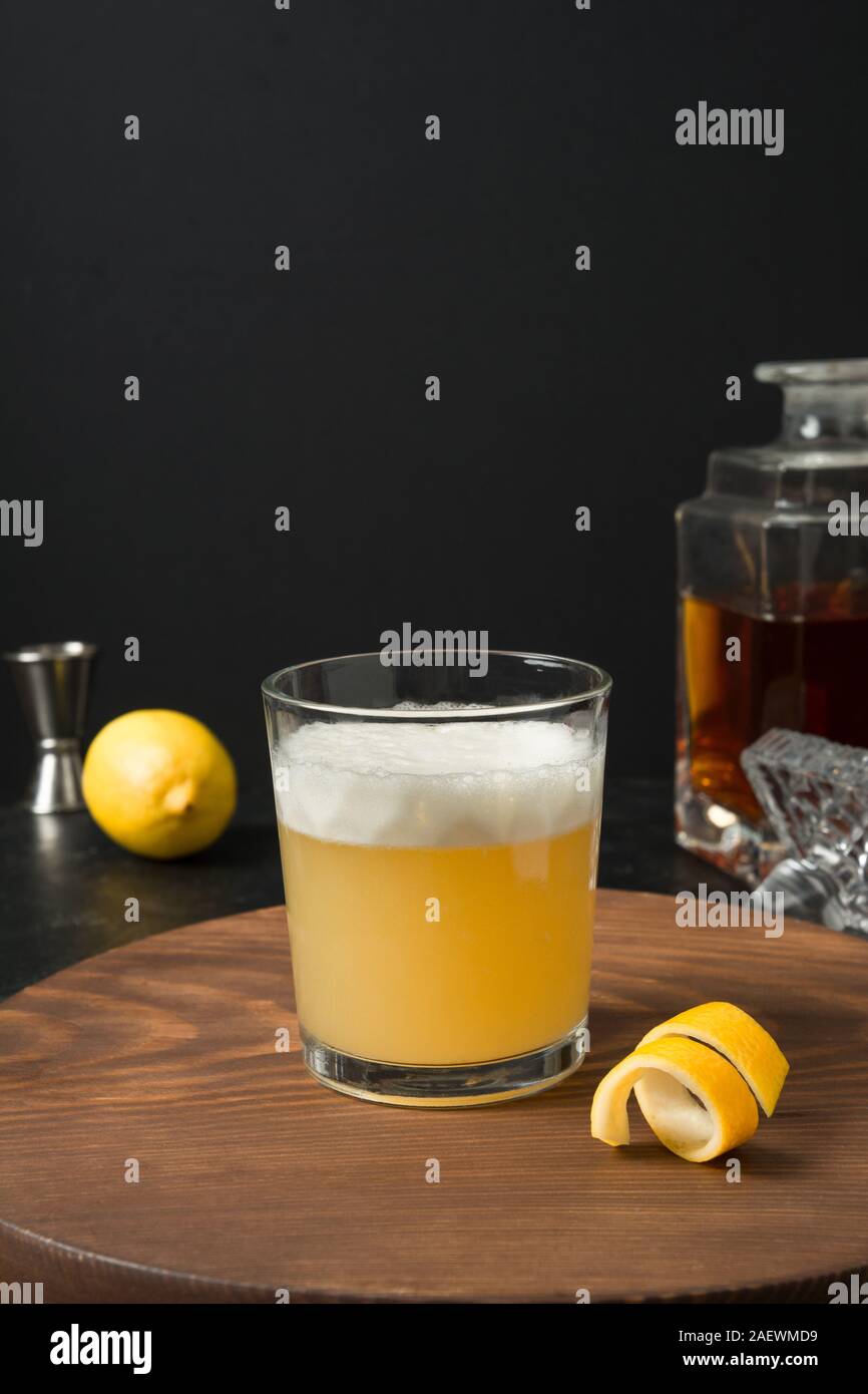 Il whiskey sour cocktail - bourbon con il succo di limone e lo sciroppo di zucchero e albume in vetro su tavola di legno sul nero. Orientamento verticale. Foto Stock