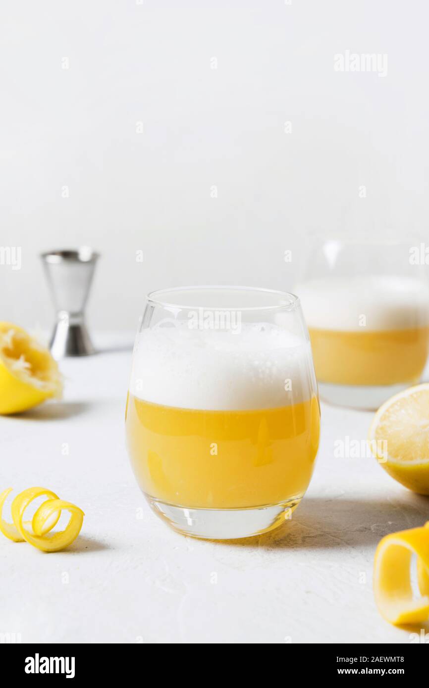 Il whiskey sour cocktail - bourbon con il succo di limone e lo sciroppo di zucchero e albume in vetro su tavola di legno sul bianco. Orientamento verticale. Foto Stock