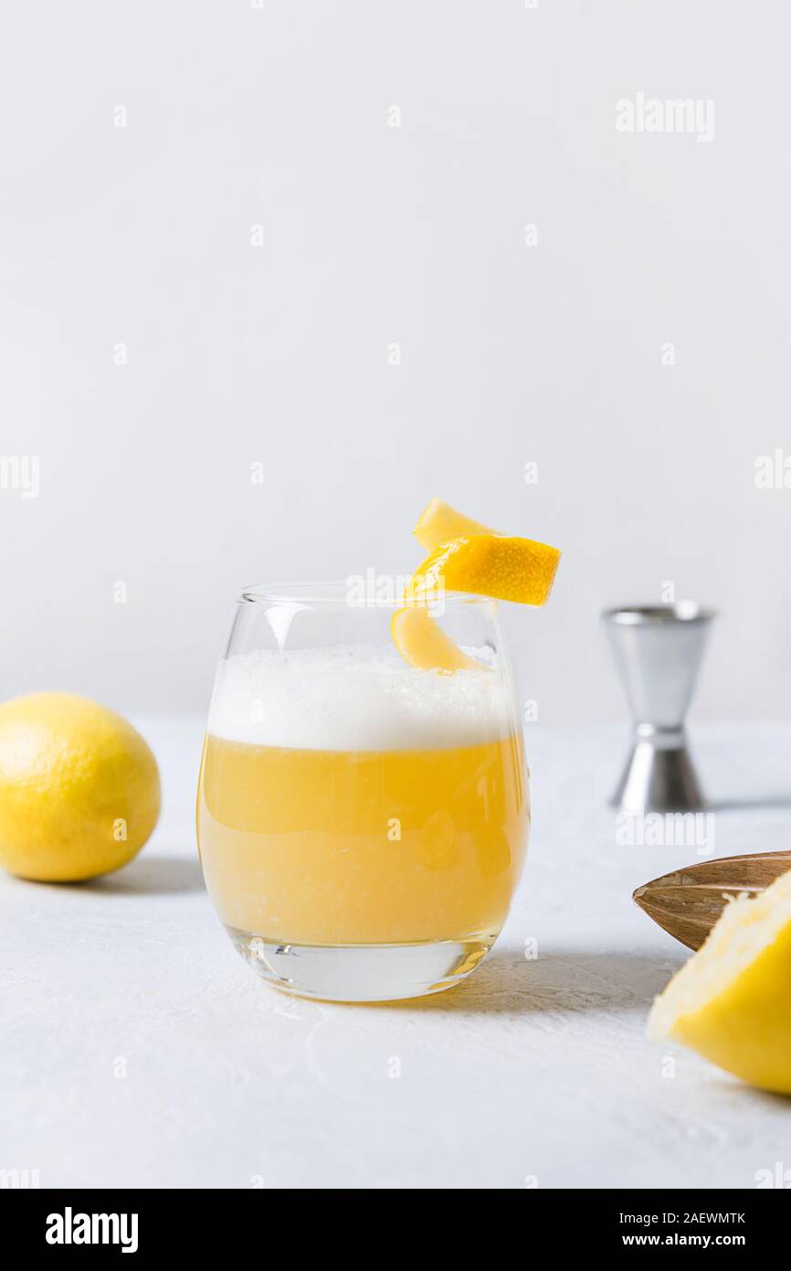 Il whiskey sour cocktail - bourbon con il succo di limone e lo sciroppo di zucchero e albume in vetro su tavola di legno sul bianco. Orientamento verticale. Foto Stock