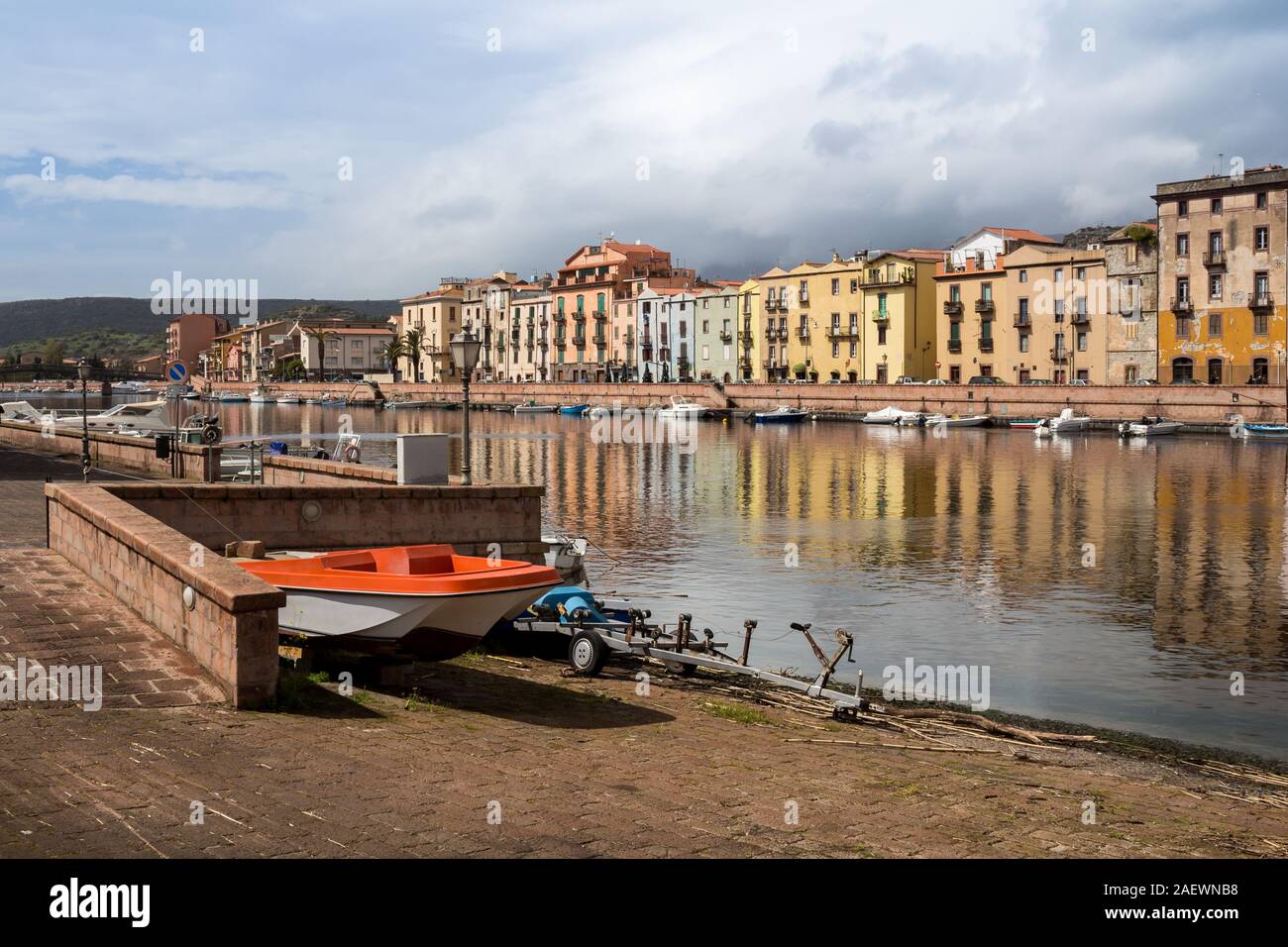 La colorata Vecchia case sulle rive del fiume Temo, con molte imbarcazioni. Rosso barca sul lungomare. Rainy cielo nuvoloso. Bosa, Sardegna, Italia. Foto Stock