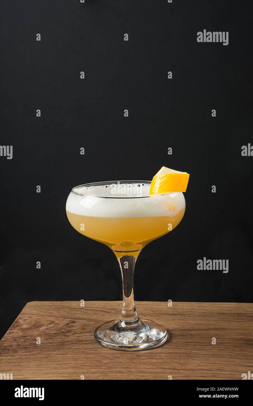 Uno shot di whiskey sour cocktail - bourbon con il succo di limone e lo sciroppo di zucchero e albume in vetro su tavola di legno sul nero. Orientamento verticale. Foto Stock