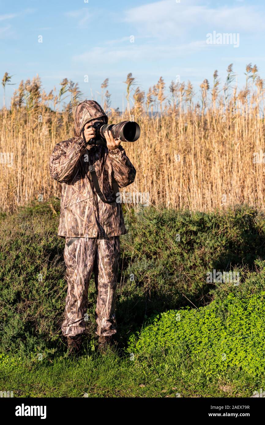 Fotografo naturalista in azione, con mimetizzazione e fotocamera, nel deserto. Foto Stock