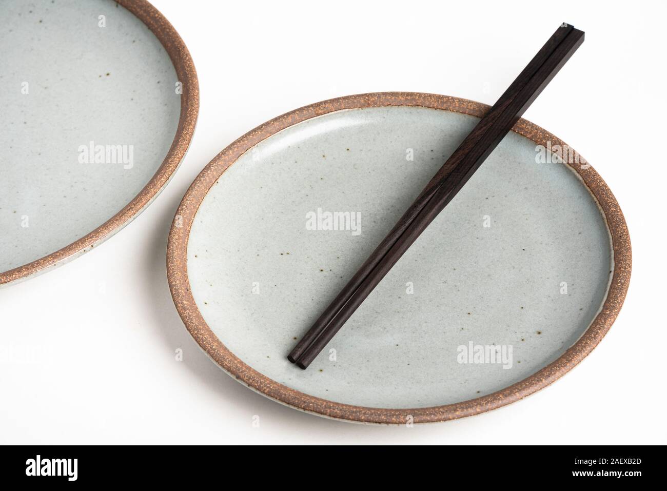 Una coppia di neri orientali bacchette di legno si appoggia su una superficie strutturata porcellanato piastra e impostare su sfondo bianco. Foto Stock