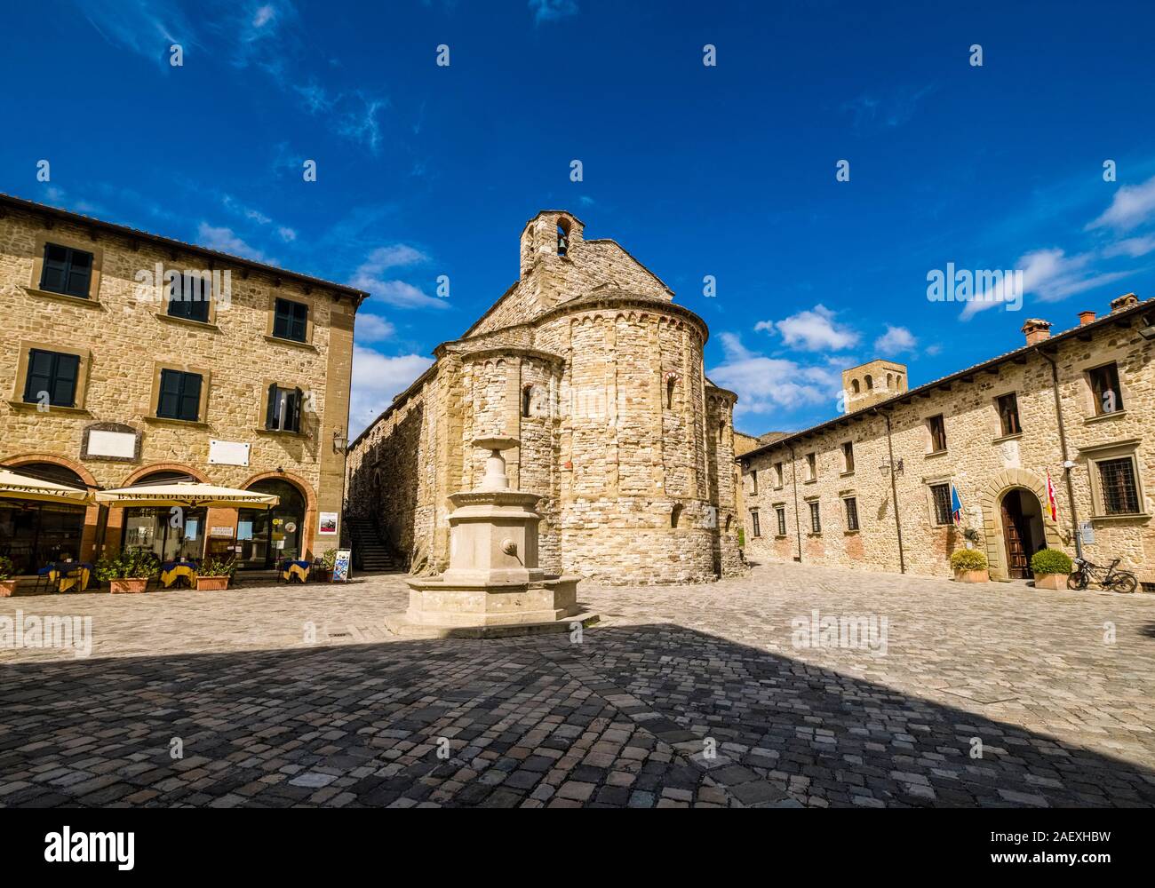La piazza principale del borgo con case in pietra, un pozzo e una chiesa Foto Stock