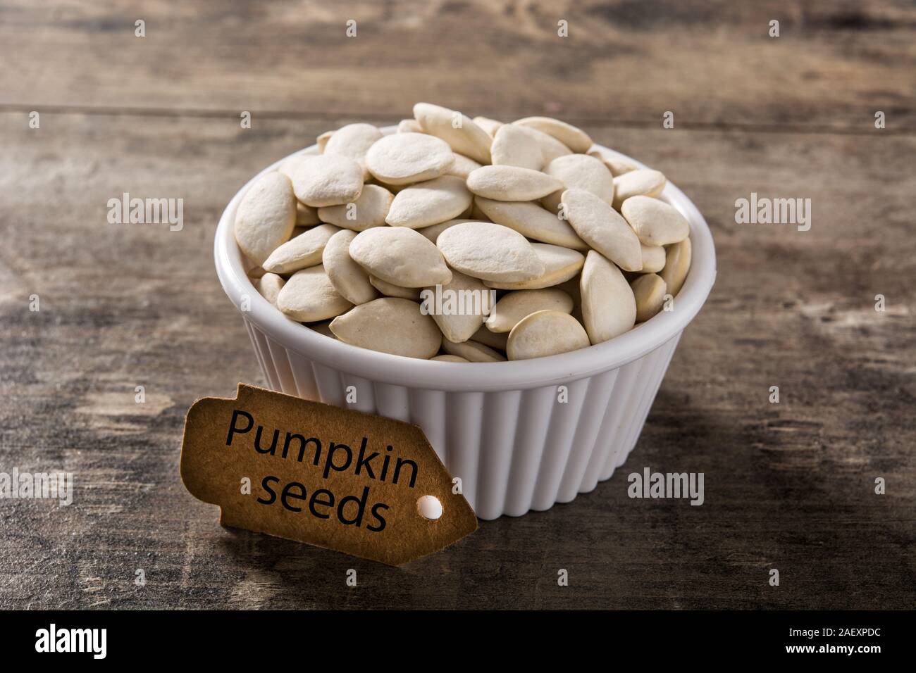 I semi di zucca in ciotola bianco su sfondo di legno. Foto Stock