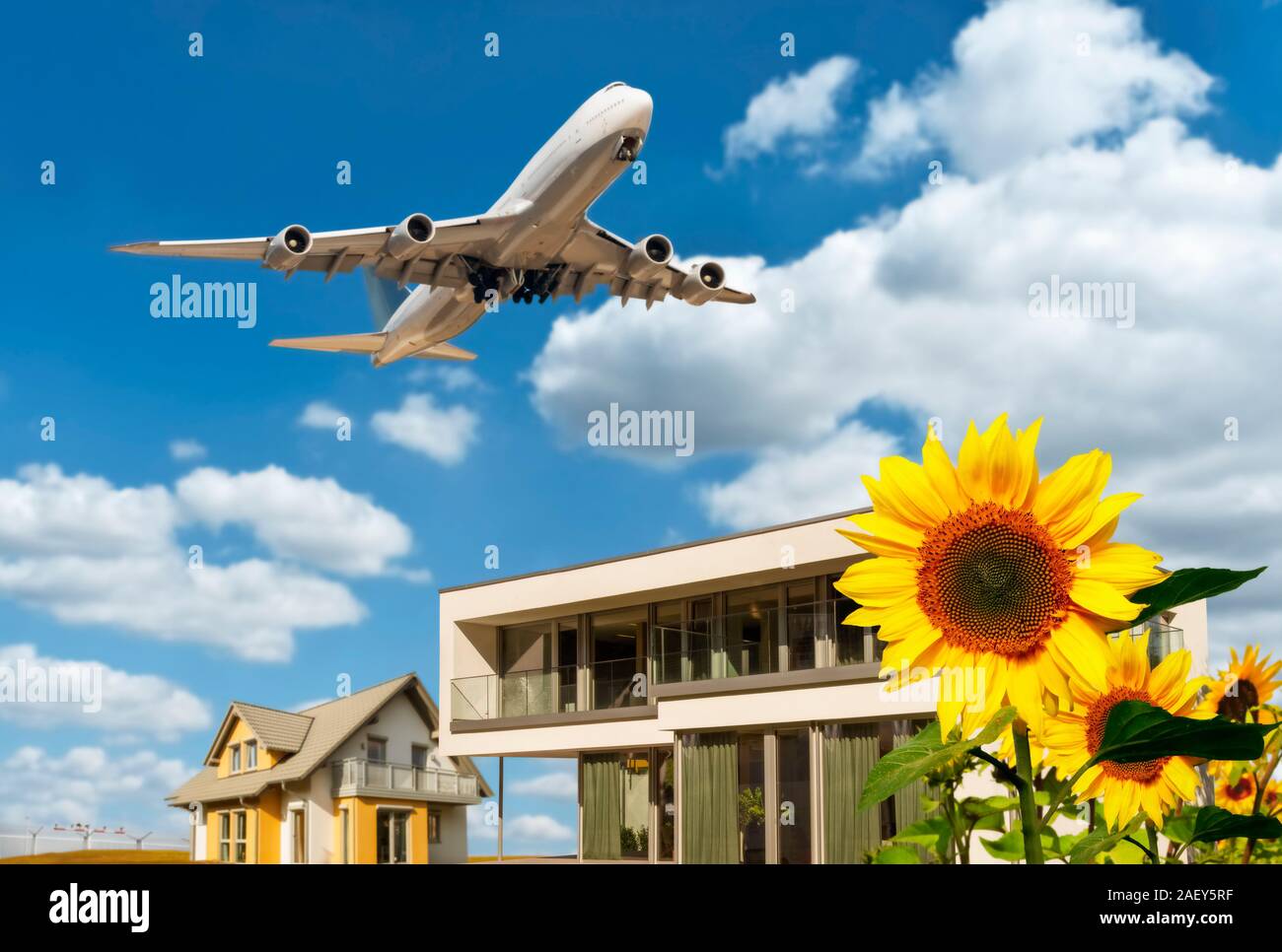 Case con girasoli, cielo blu e nuvole e aereo in background Foto Stock
