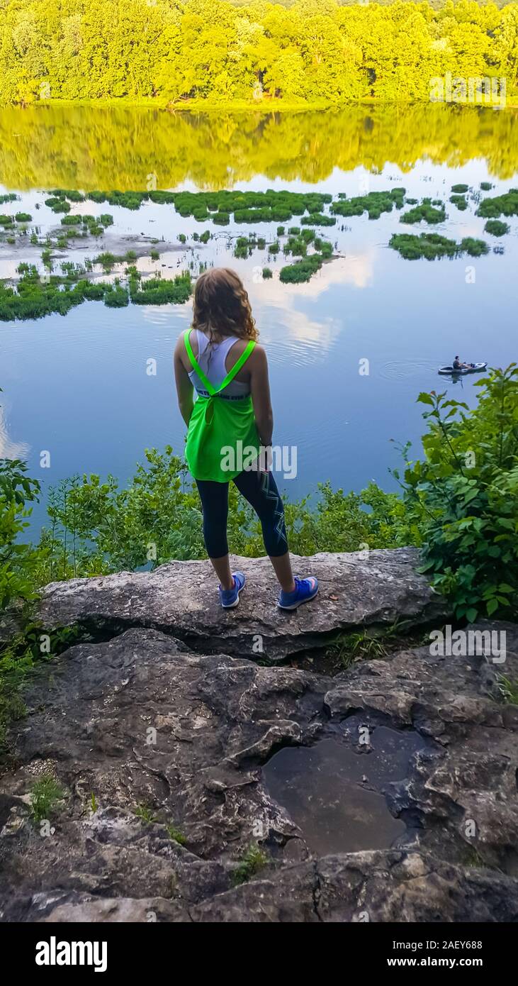 Un adolescente sorge su un promontorio in abbigliamento atletico affacciato su un lago. Foto Stock