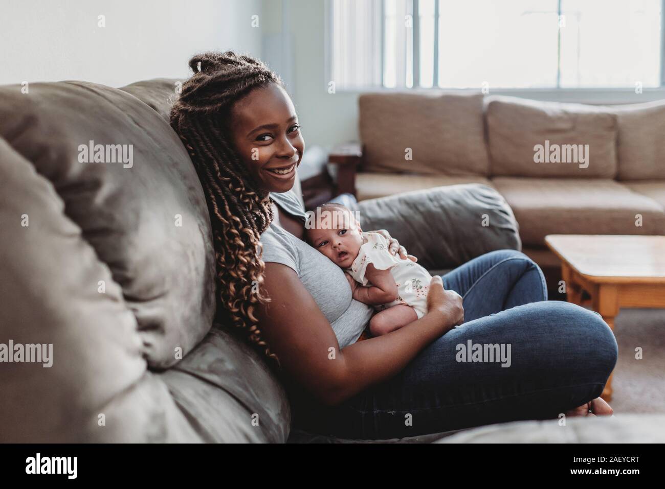 Mid-30â€™s mom etnico con lunghe trecce sul lettino holding multirazziale baby Foto Stock