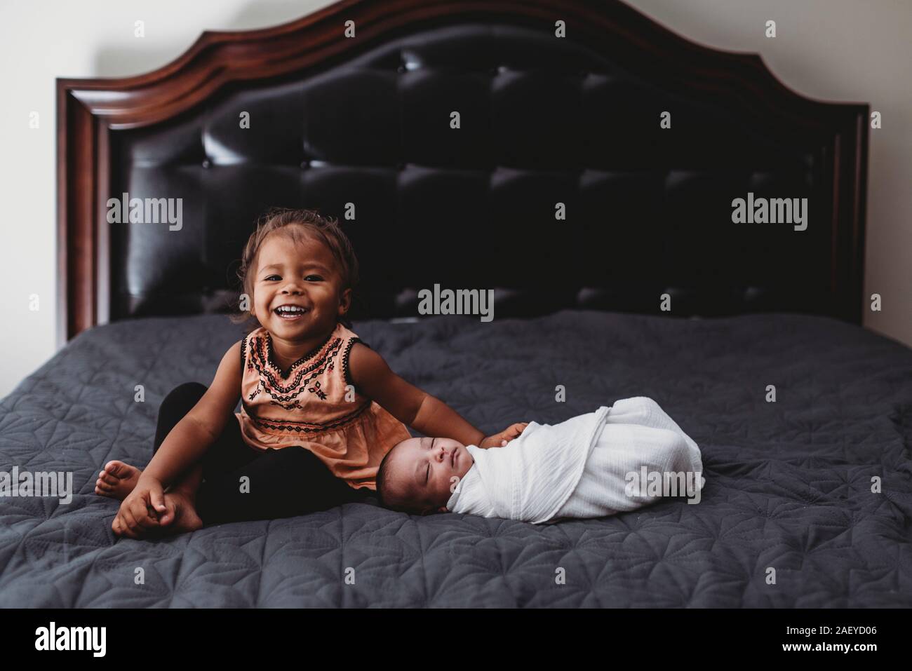 Sorridente biracial 2 yr old girl sul letto con i gemelli neonati Foto Stock