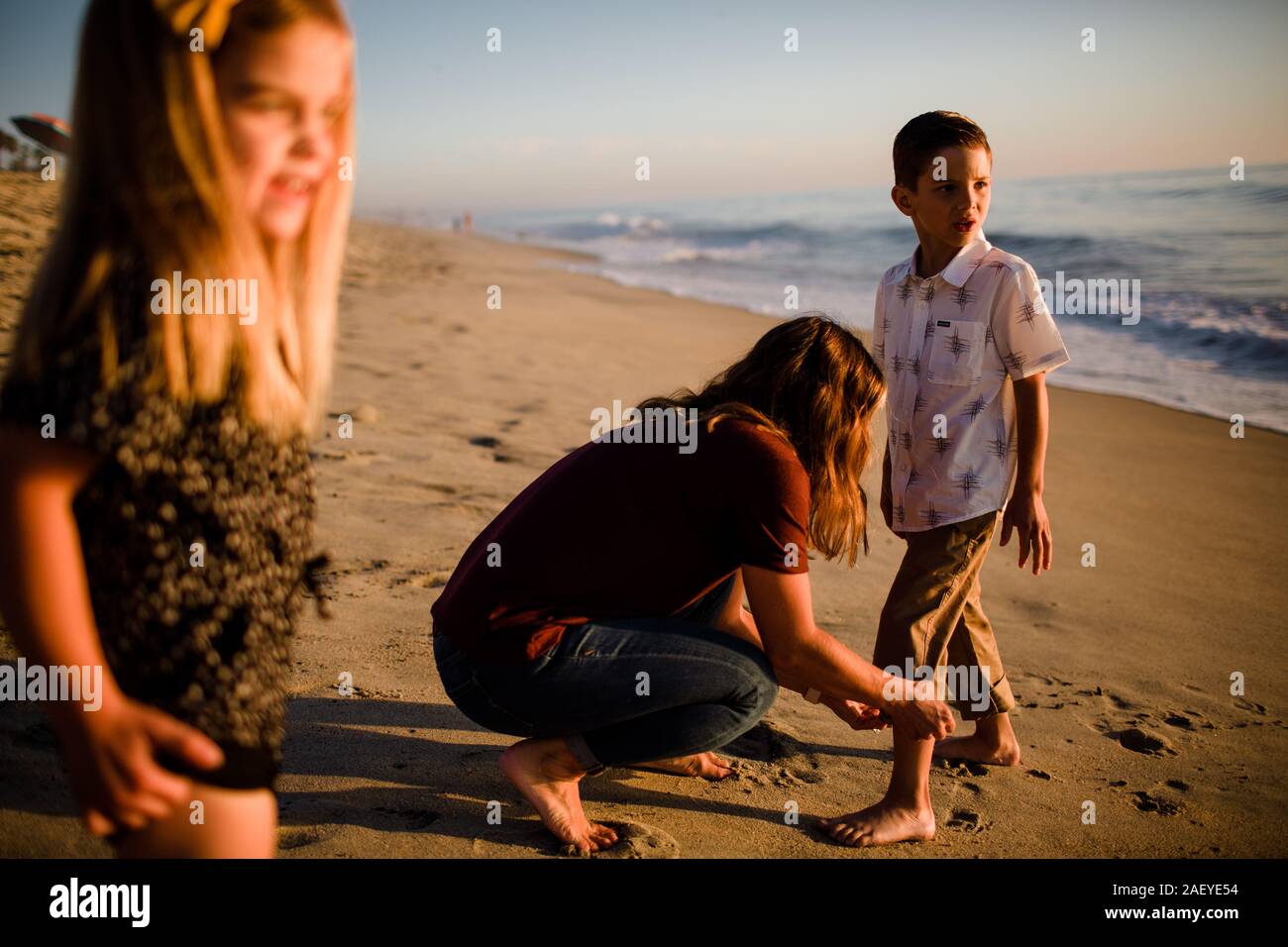 Mom figlio taglio pantalone sulla spiaggia mentre la sorella attende Foto Stock