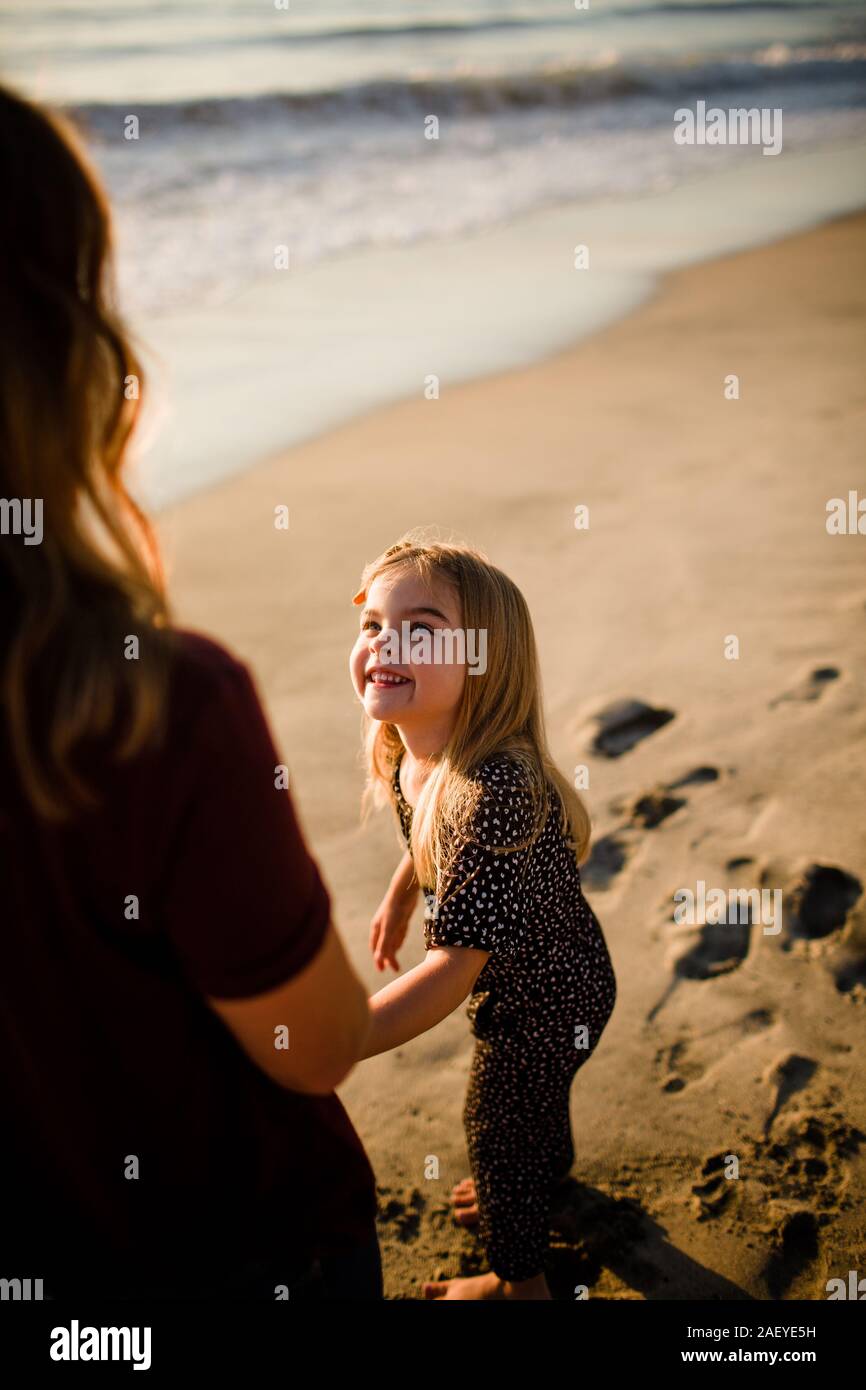 Figlia sorridente al Mom sulla spiaggia al tramonto Foto Stock