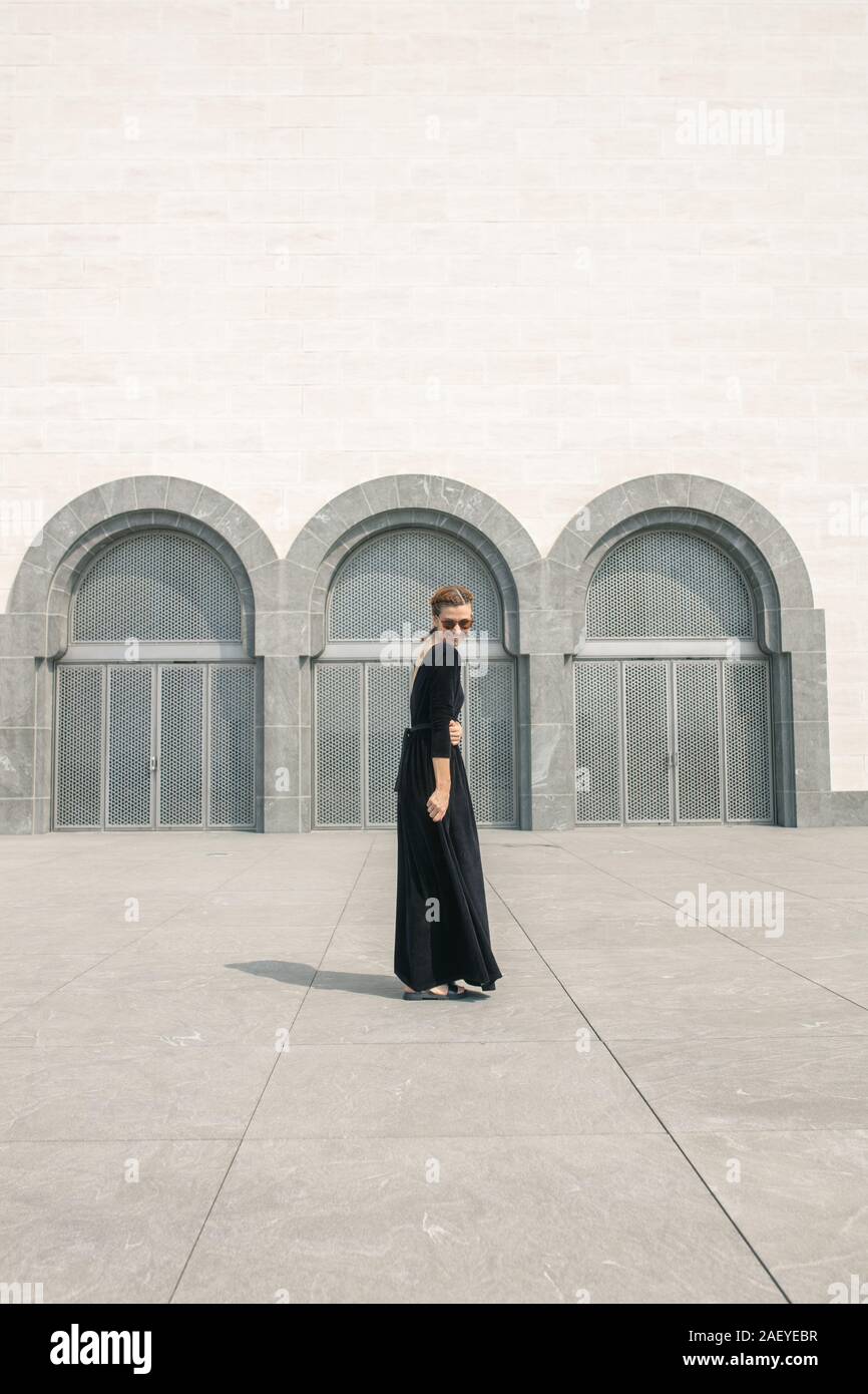 Giovane donna in Lungo abito nero in posa davanti le porte dell'edificio Foto Stock