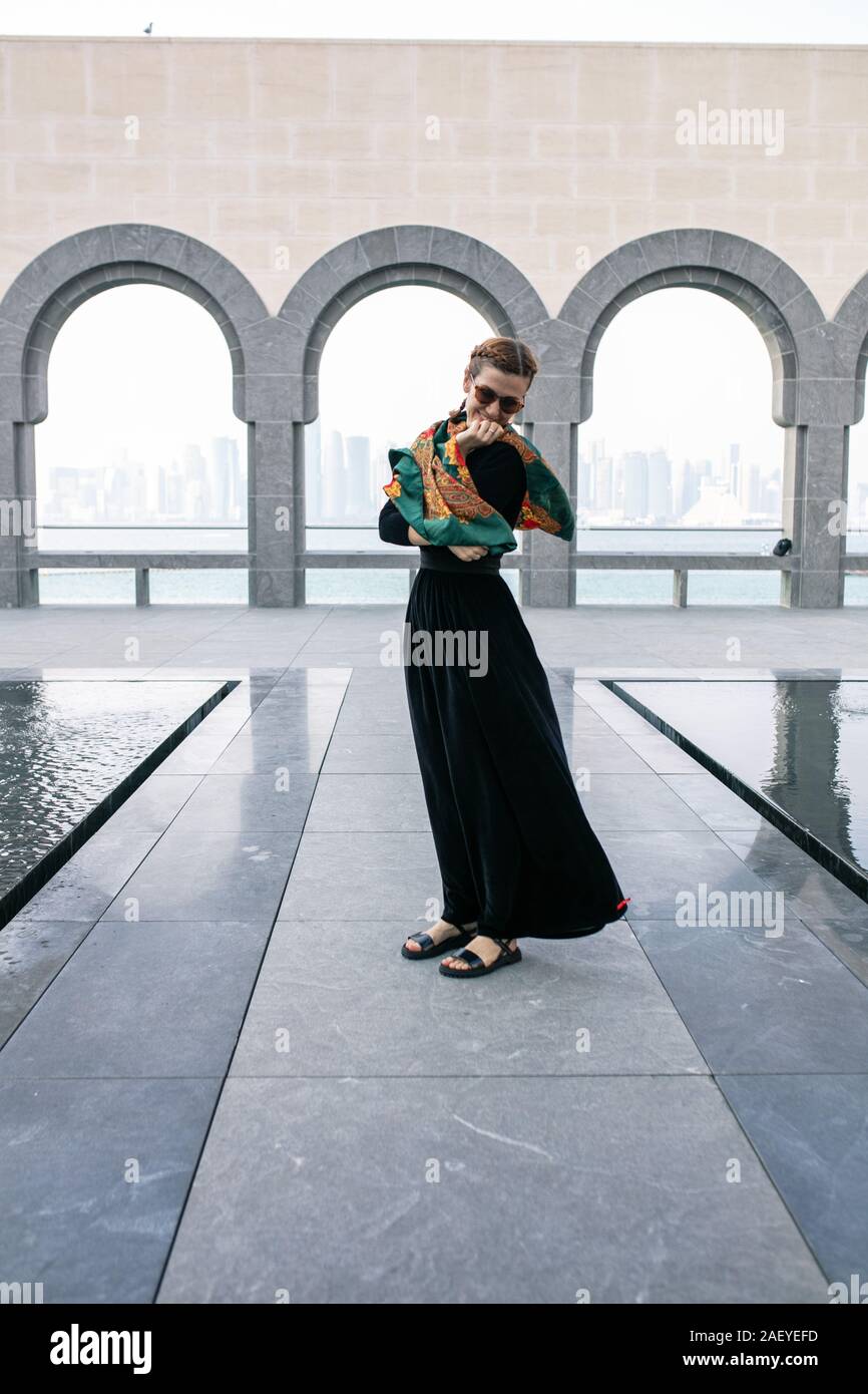 Giovane donna in piedi in Lungo abito nero avvolto in sciarpa colorata Foto Stock