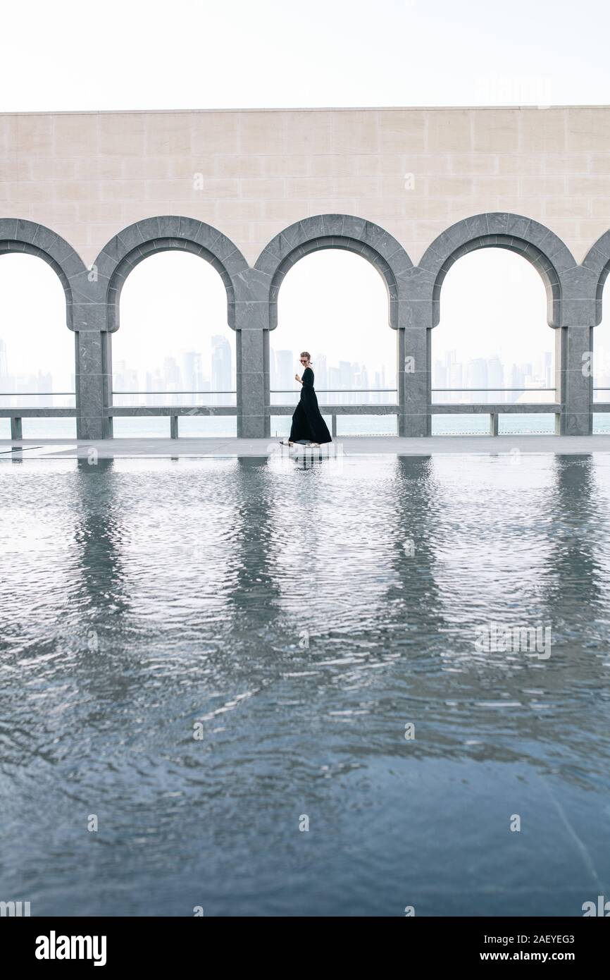 Giovane donna in Lungo abito nero a piedi dal pool nel museo Foto Stock