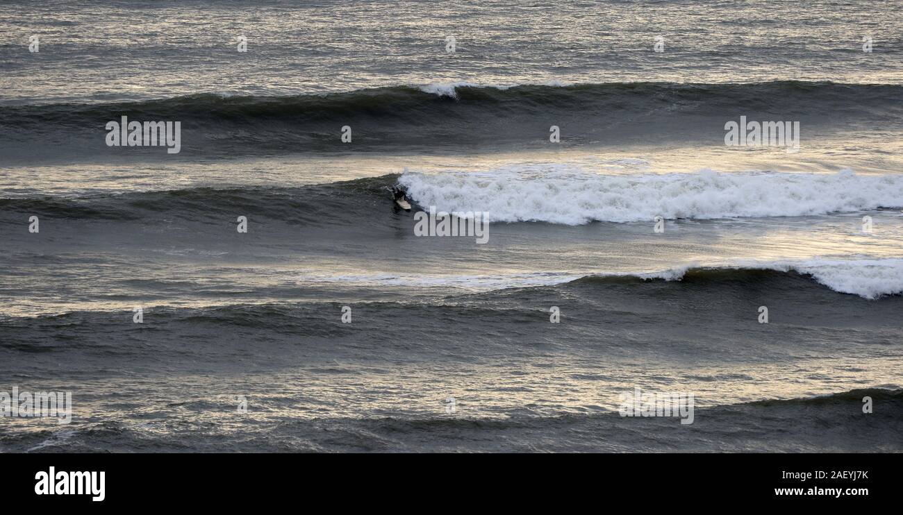 Un surfista effettuare la sua scelta dell'onda e le piastre o decolla su un point break a onda Langland Bay nel Galles del Sud Foto Stock