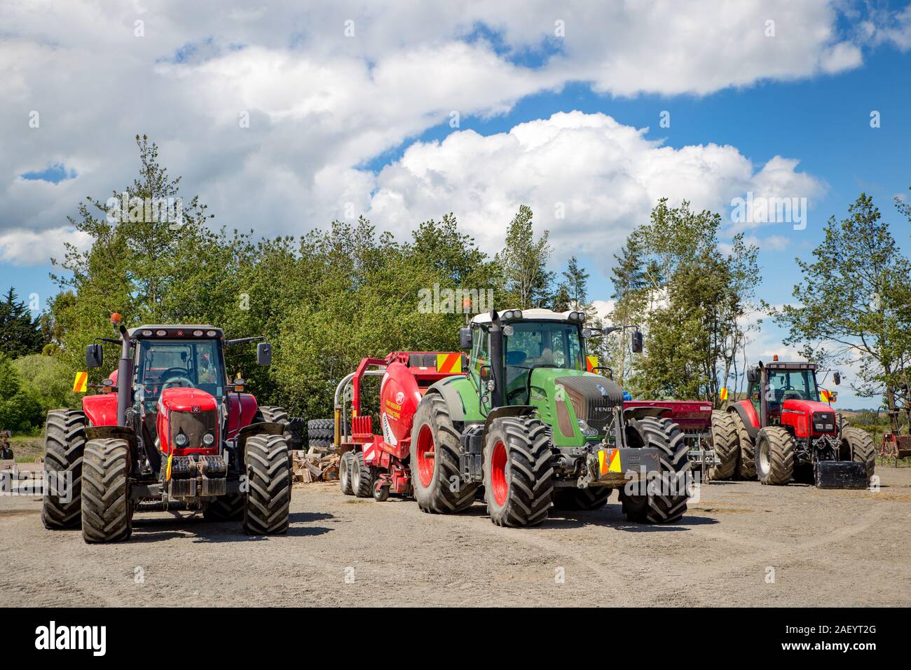 Otago, Nuova Zelanda, 8 Dicembre 2019: tre trattori con la falciatura e imballaggio macchine parcheggiate fino a un appaltatore's Yard tra lavori di fattoria Foto Stock