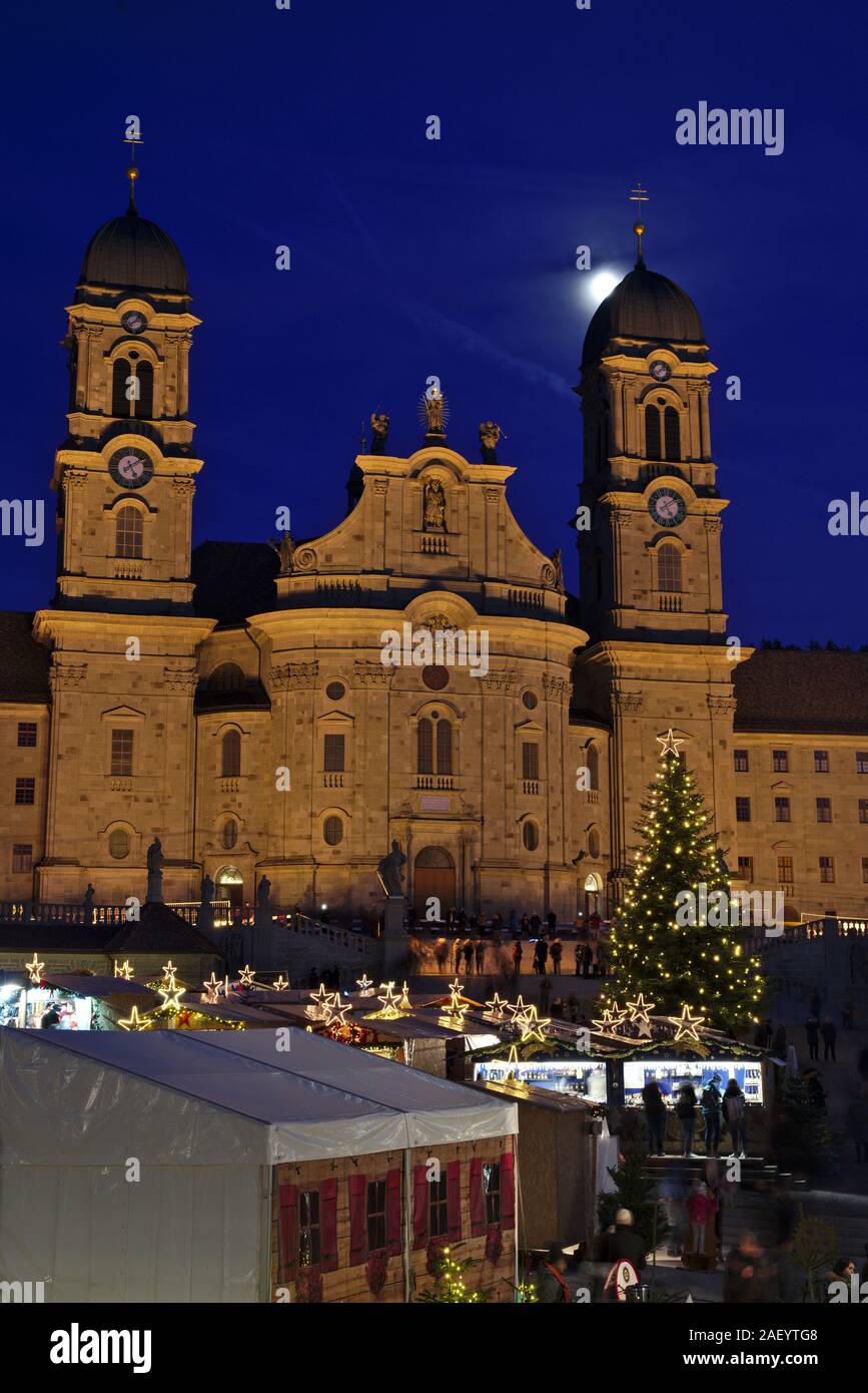 Einsiedler Weihnachtsmarkt (mercatino di Natale) nella parte anteriore del monastero di Einsiedeln all'alba con un albero di natale, cabine e la luna brilla sopra. Foto Stock