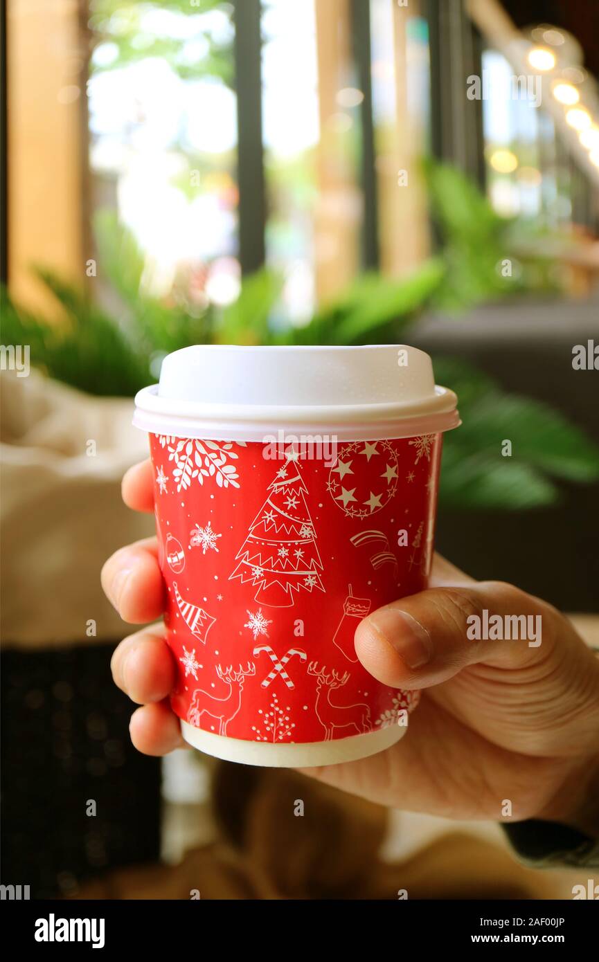 L'immagine verticale di mano d'uomo tenendo un rosso e bianco da asporto tazza di caffè Foto Stock