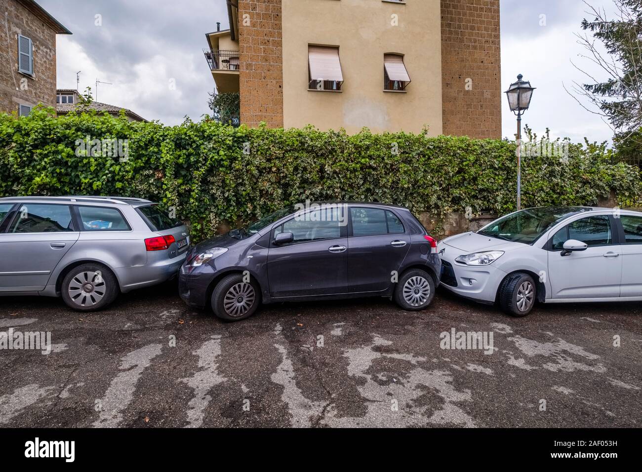 Un auto nera bloccati tra due altre vetture in uno spazio di parcheggio in corrispondenza di un bordo strada Foto Stock