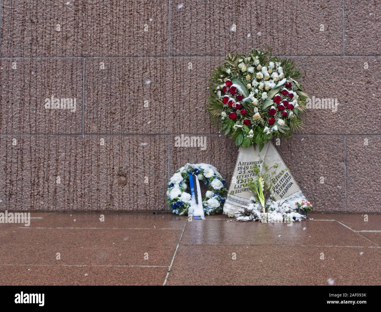 Ghirlande di fiori con archetto messo di fronte al monumento della libertà in un giorno di neve a Riga per commemorare il opressed politico durante l'occupazione sovietica# Foto Stock