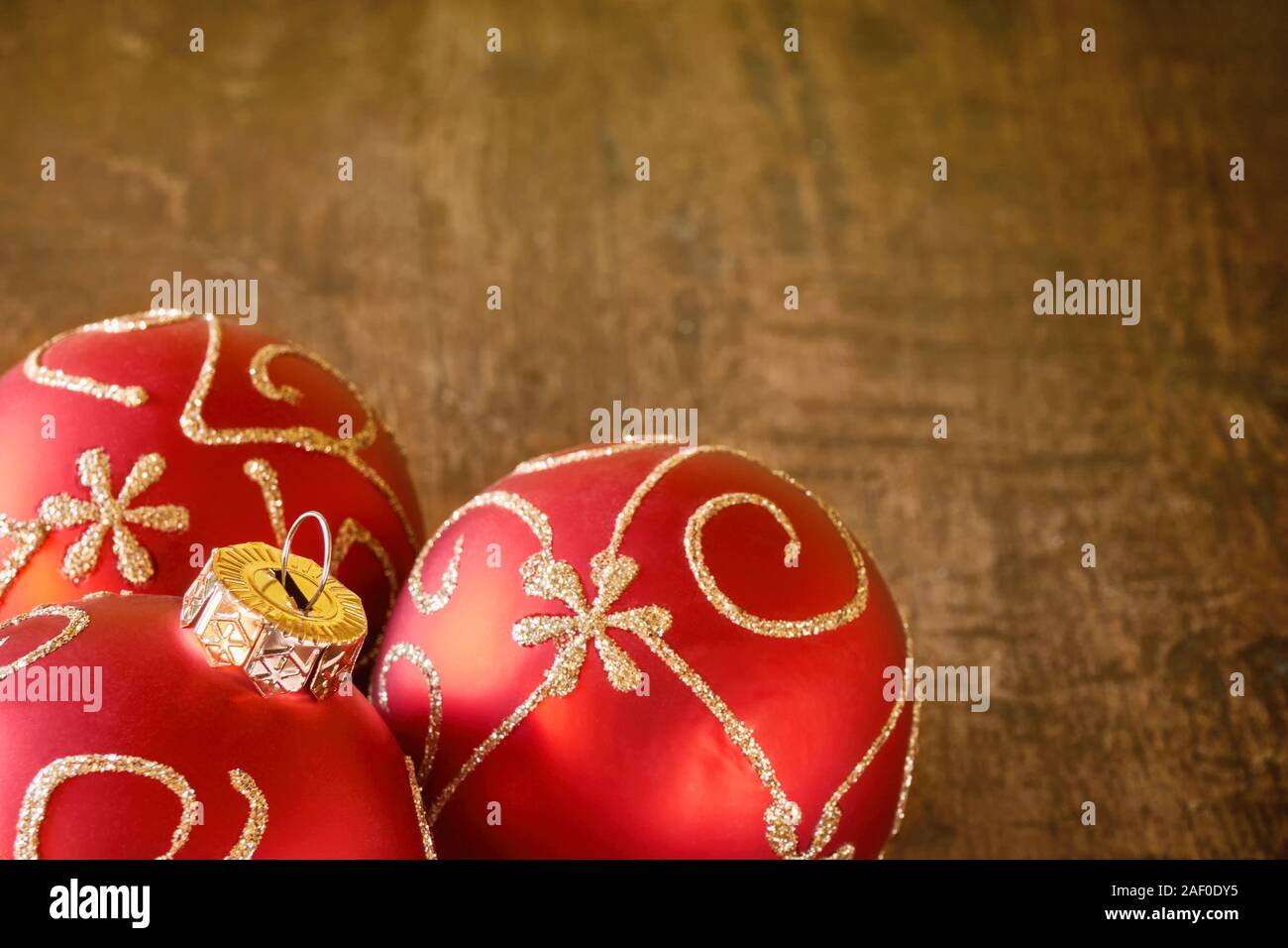 Close-up di tre mat rosso palle di Natale con golden swirly decorazione sul vecchio dark tavolo in teak con copia spazio per un Natale sfondo o carta. Foto Stock