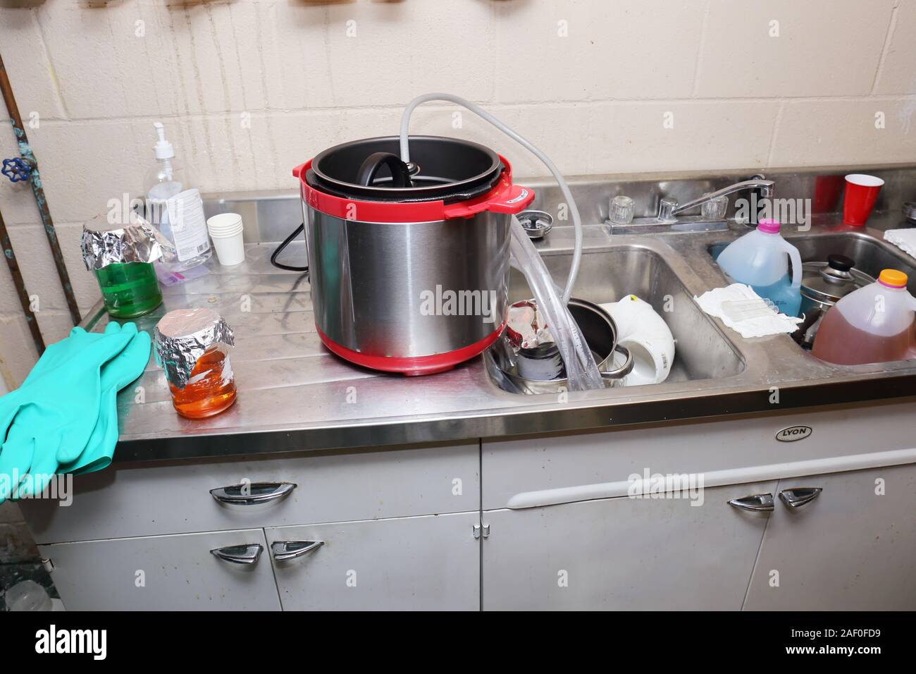 In casa la sintesi di un composto chimico, probabilmente qualcosa di illegale, in un seminterrato sink utilizzando una pentola a pressione, i tubi flessibili e un vaso in una pentola di acqua condizionata Foto Stock