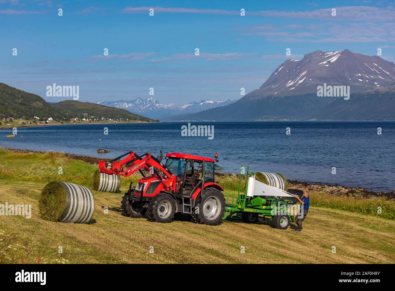 BAKKEJORD, KVALØYA ISLAND, Troms, Norvegia - contadino e trattore agricolo con le balle di fieno, sul fiordo Straumsfjorden. Foto Stock