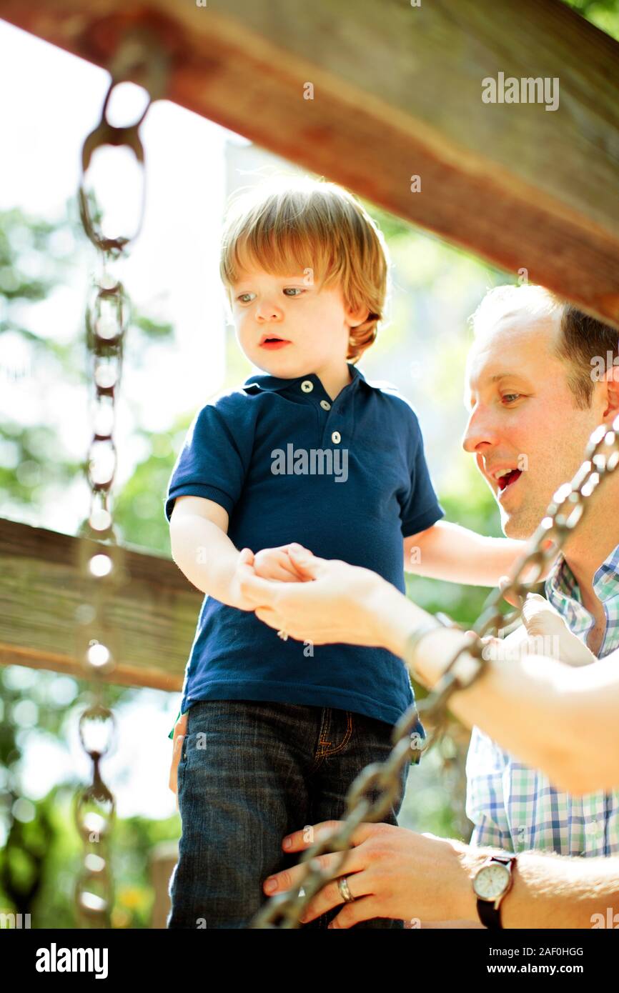 Papà tenendo figli mano sulla struttura di gioco Foto Stock