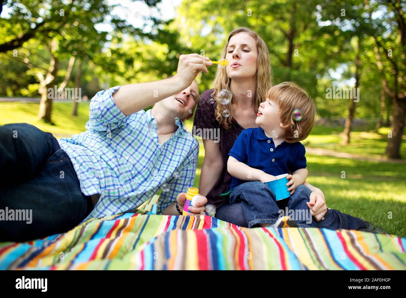 Famiglia soffiare bolle con figlio nel parco Foto Stock