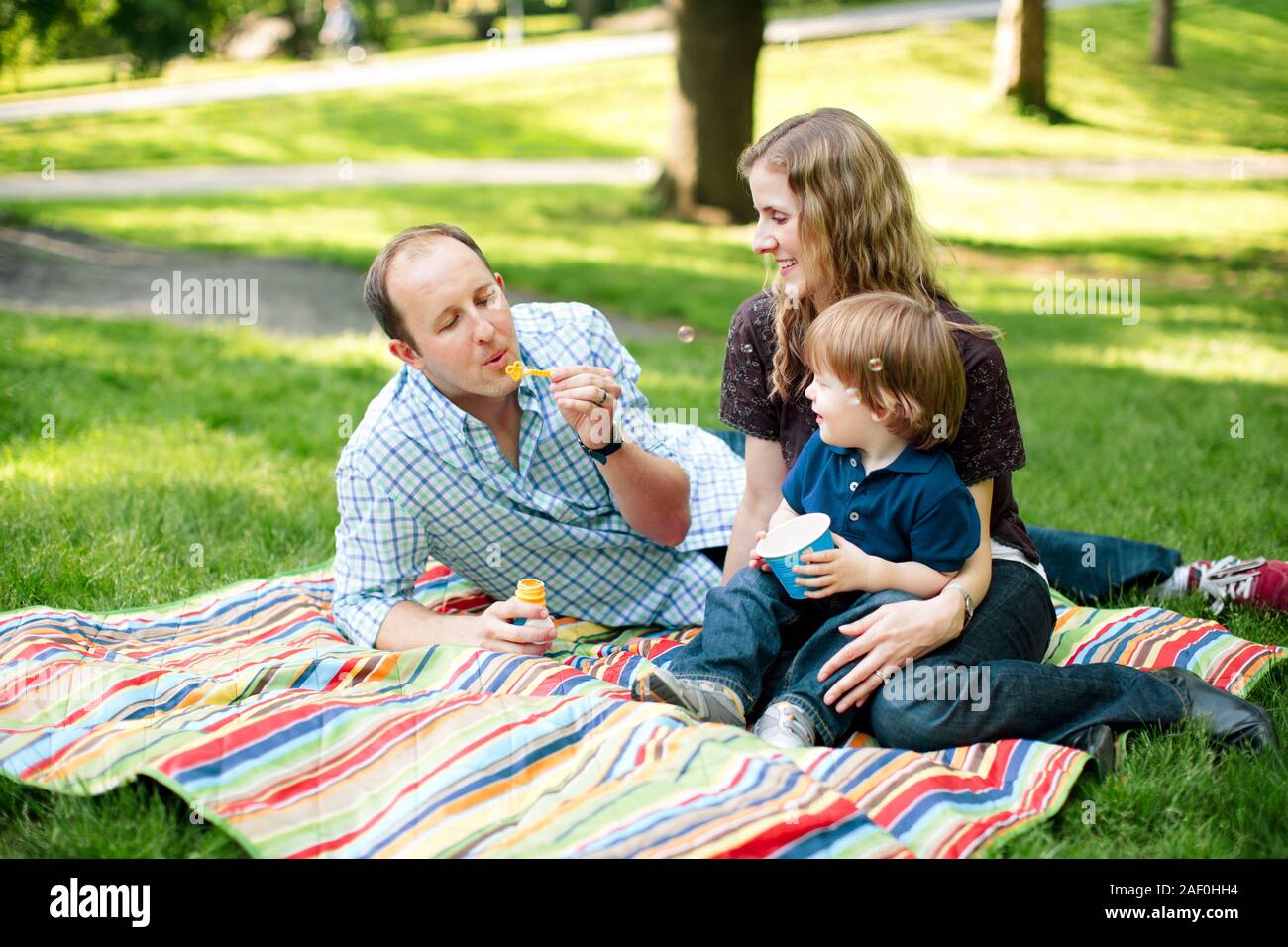 Famiglia soffiare bolle con figlio nel parco Foto Stock