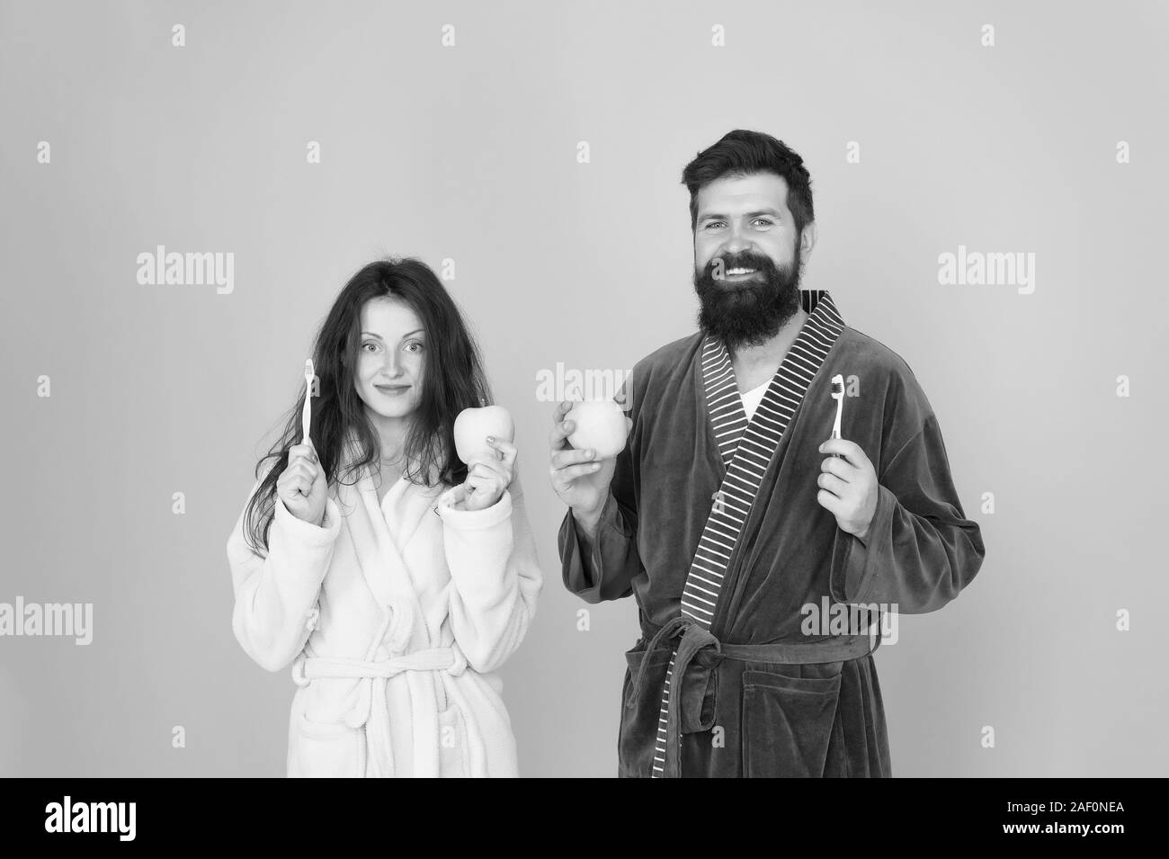 Avendo una sana e robusta dentatura. mattina di routine. personal care in mattina. matura in accappatoio toelettatura. uomo barbuto e ragazza sorriso sano. famiglia giovane tenere apple con uno spazzolino da denti. Foto Stock