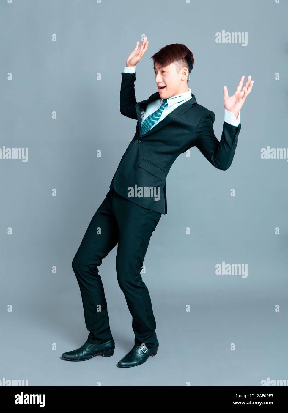 Spaventata giovane uomo d affari in piedi davanti a uno sfondo grigio Foto Stock